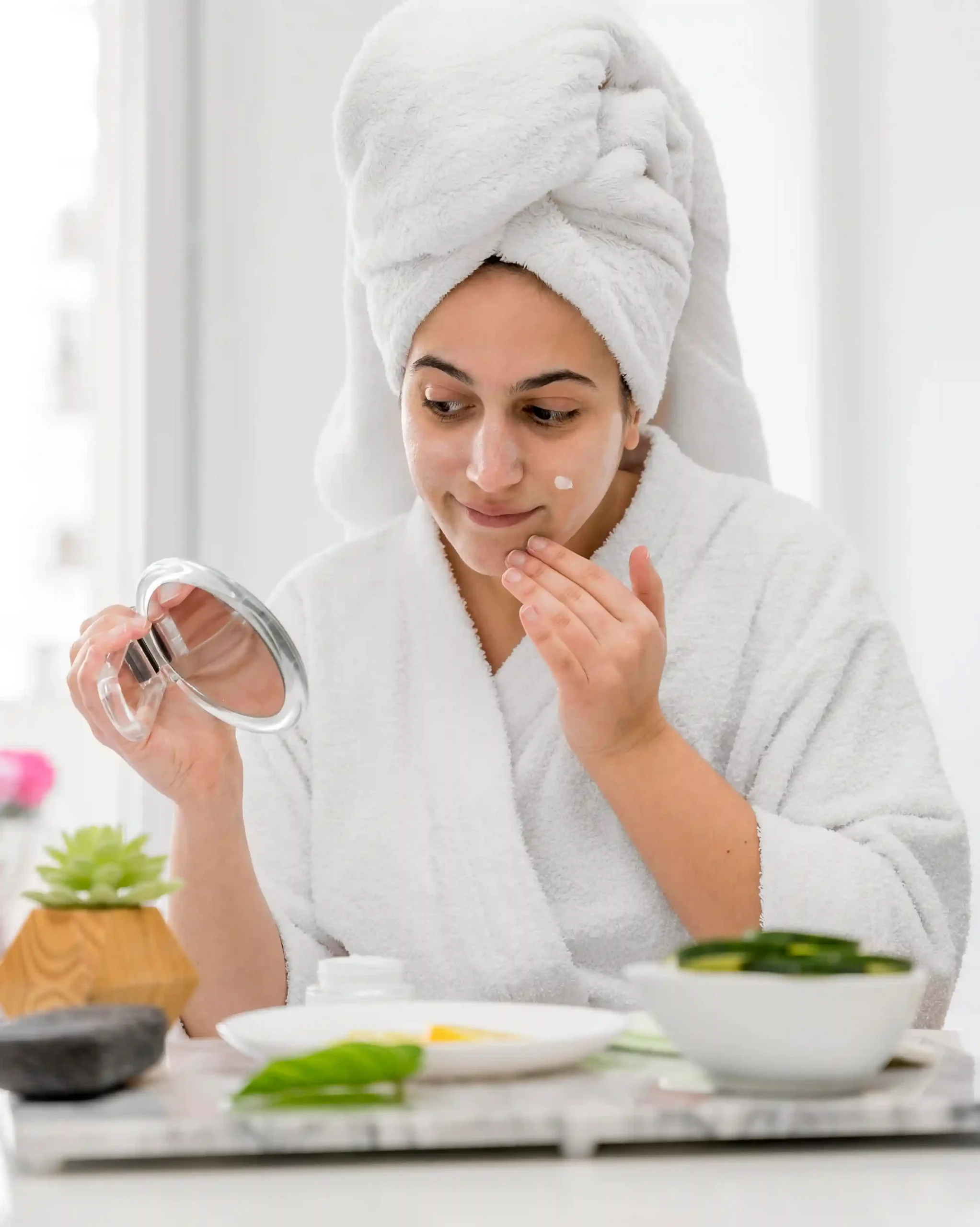 Woman applying face cream in a white robe, representing daily skin barrier support.
