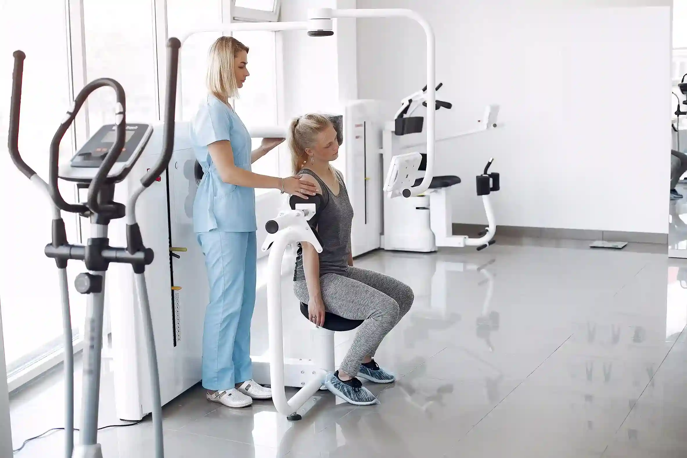 A medical professional assists a patient with a personal fitness program using gym equipment.