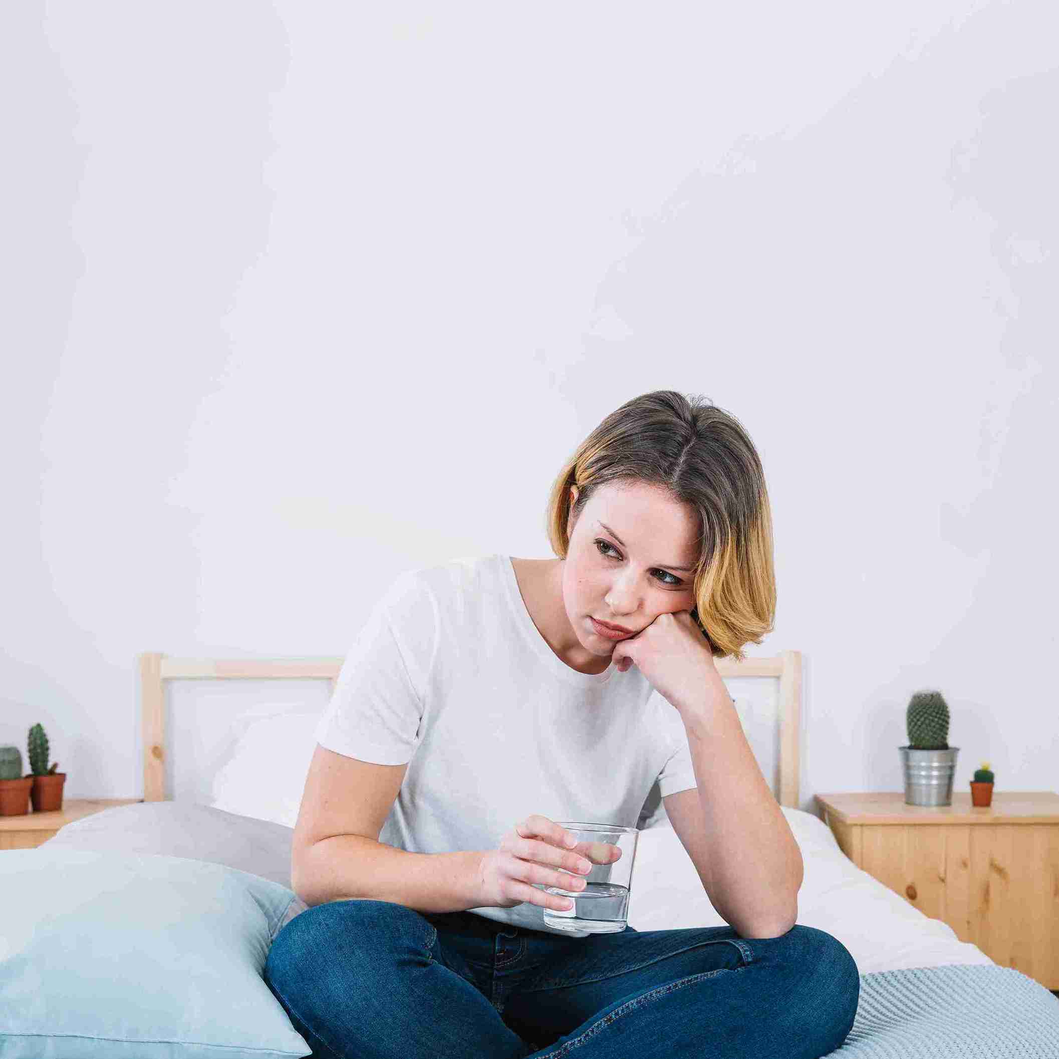 Woman sitting on a bed with a glass of water, highlighting UTI symptoms and hydration.